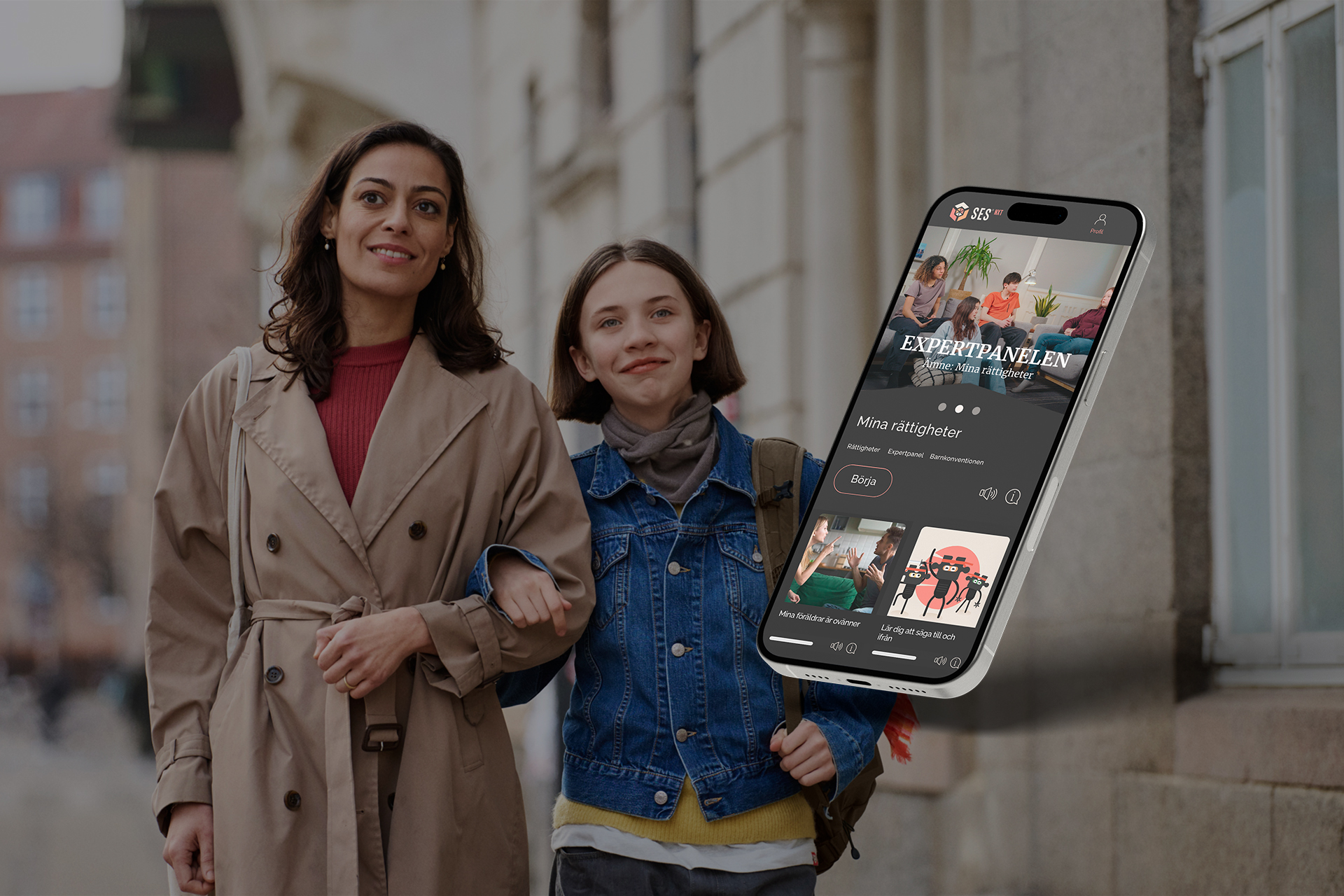 A woman and young lady walk hand in hand down a street with a smart phone showing SES Family content imposed on the foreground